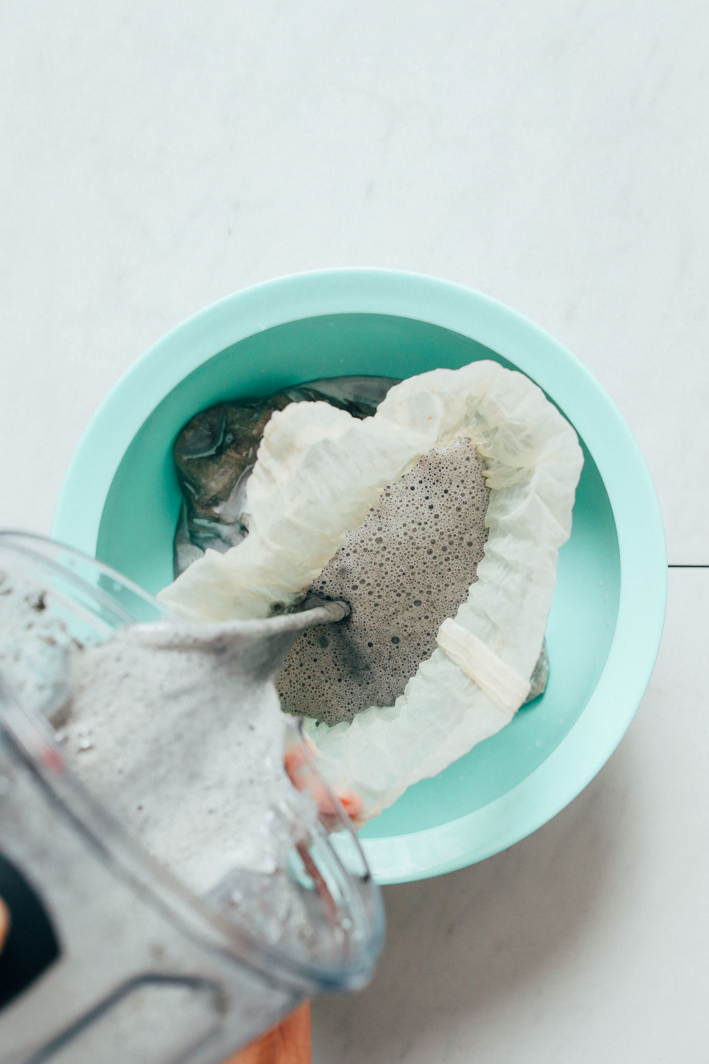Pouring a blender of Black Sesame Milk through a nut milk bag