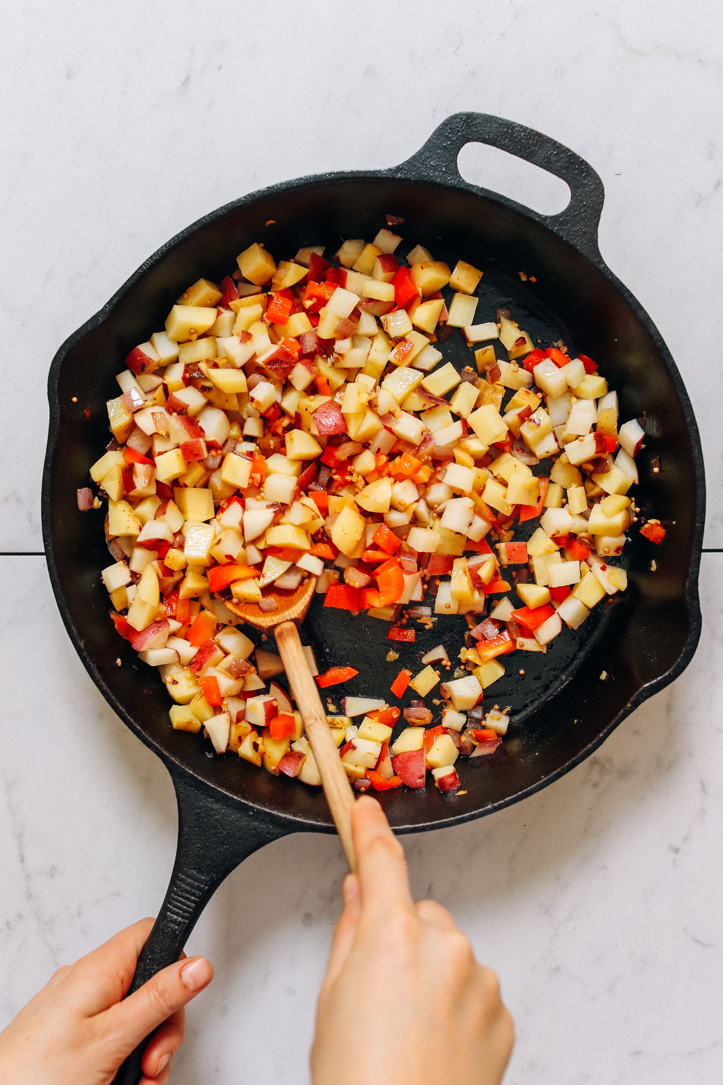 Using a wooden spoon to stir ingredients for Potato Aloo Sabzi in a cast-iron skillet
