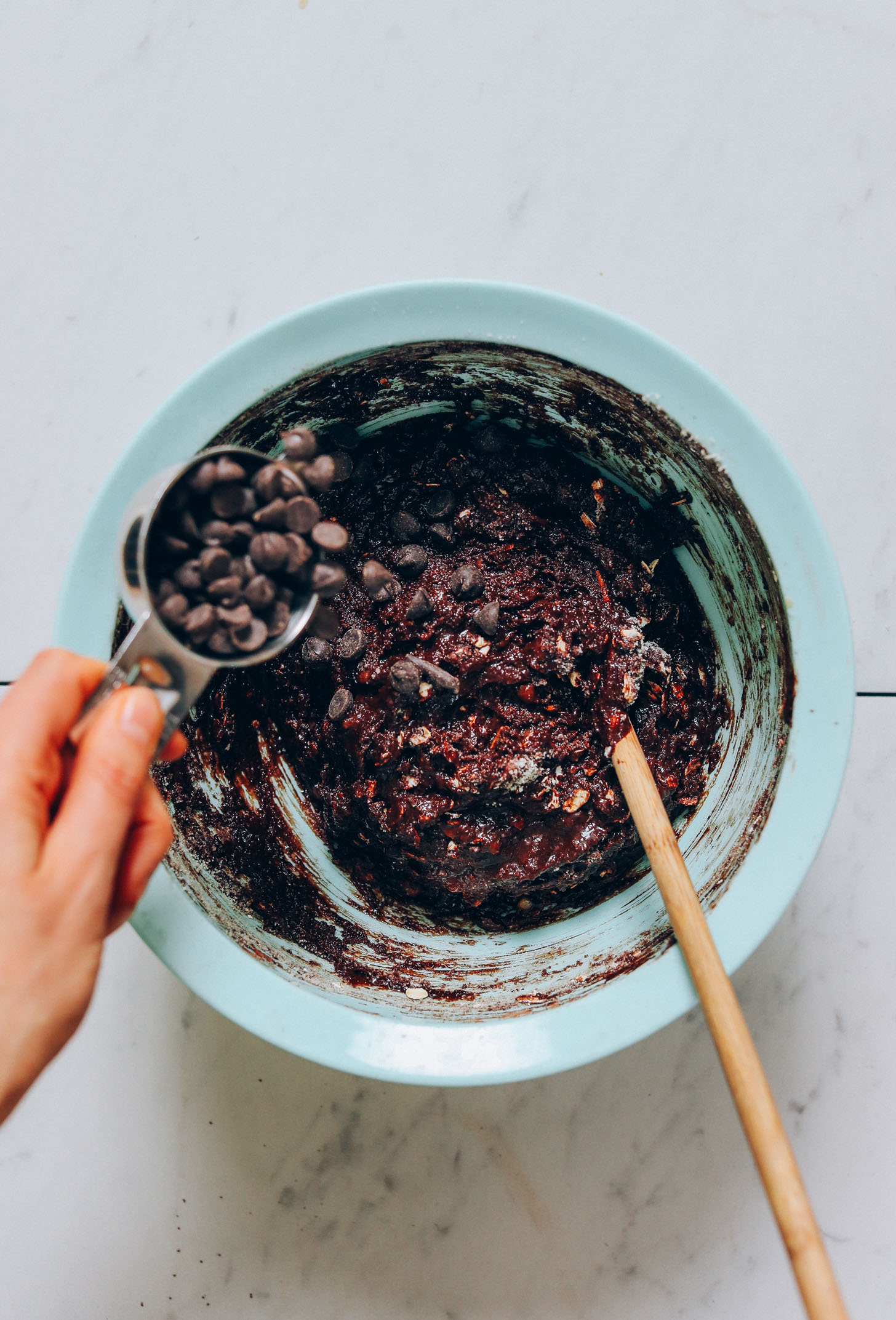 Pouring chocolate chips into a bowl of Banana Chocolate Muffin batter