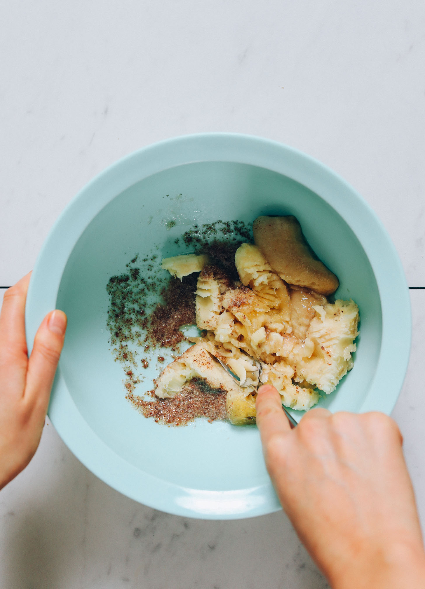 Using the back of a fork to mash banana and flax seed meal in a large mixing bowl