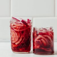 Two jars of Quick Pickled Onions on a white tile background