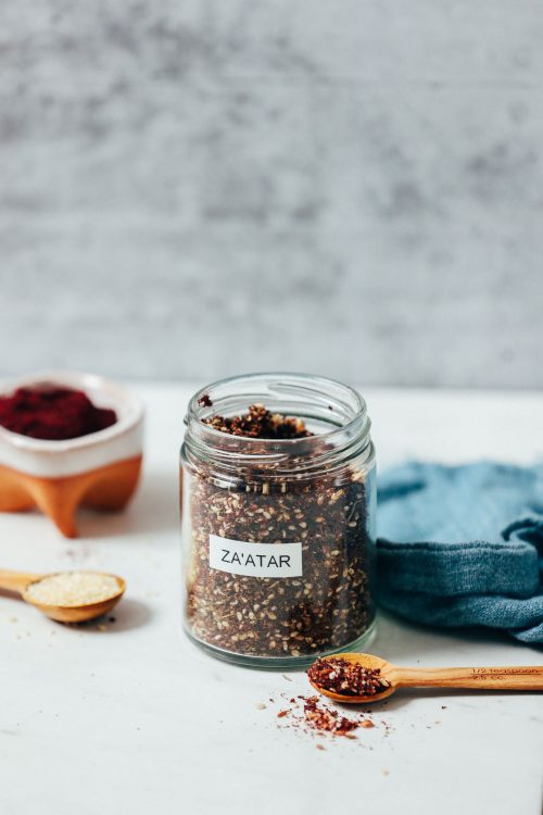 Jar and bowl of homemade za'atar seasoning beside ingredients used to make it