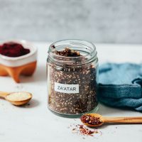 Spoonfuls of sesame seeds and za'atar next to a jar