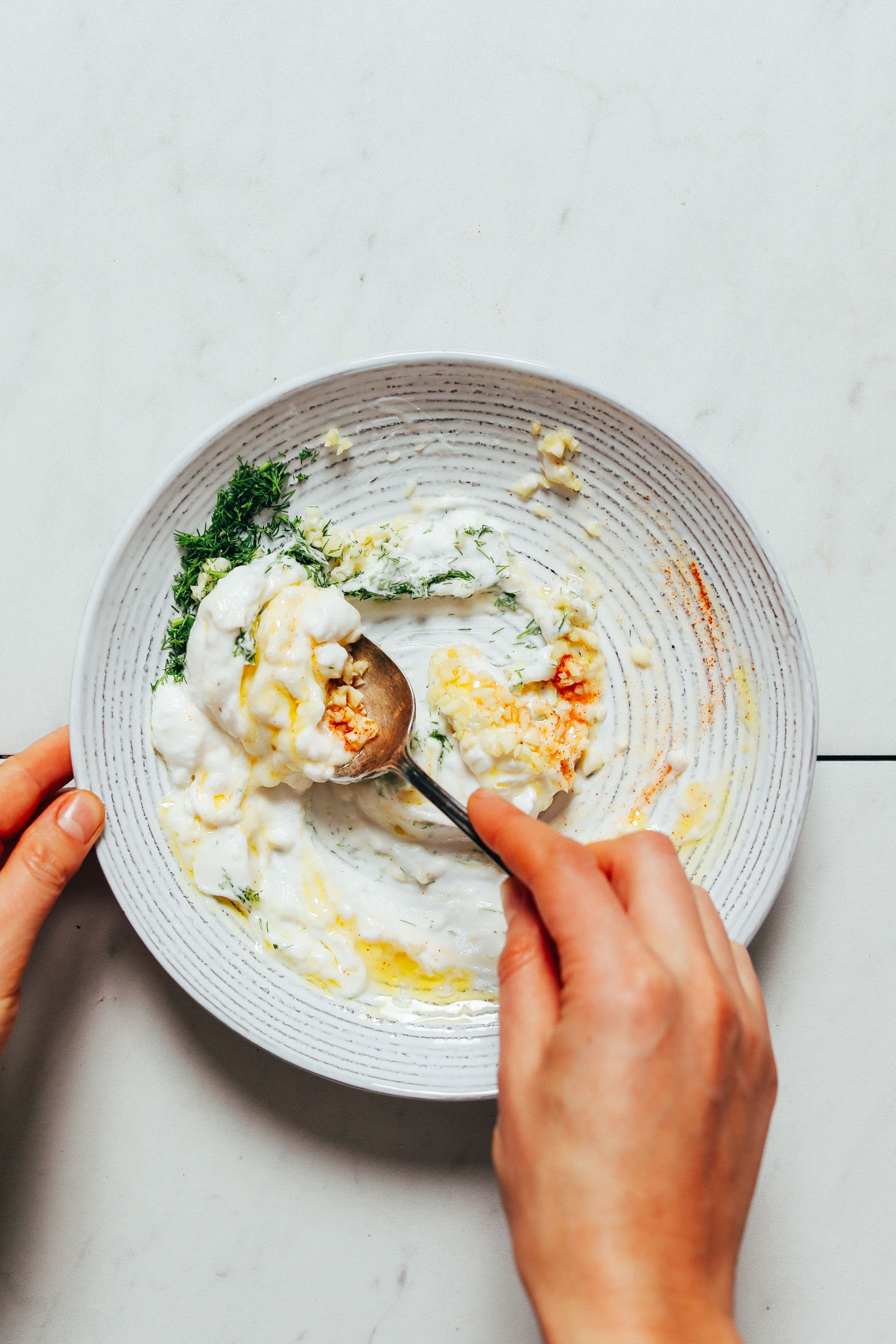 Using a spoon to stir yogurt with lemon juice, olive oil, and other ingredients for a delicious dill sauce