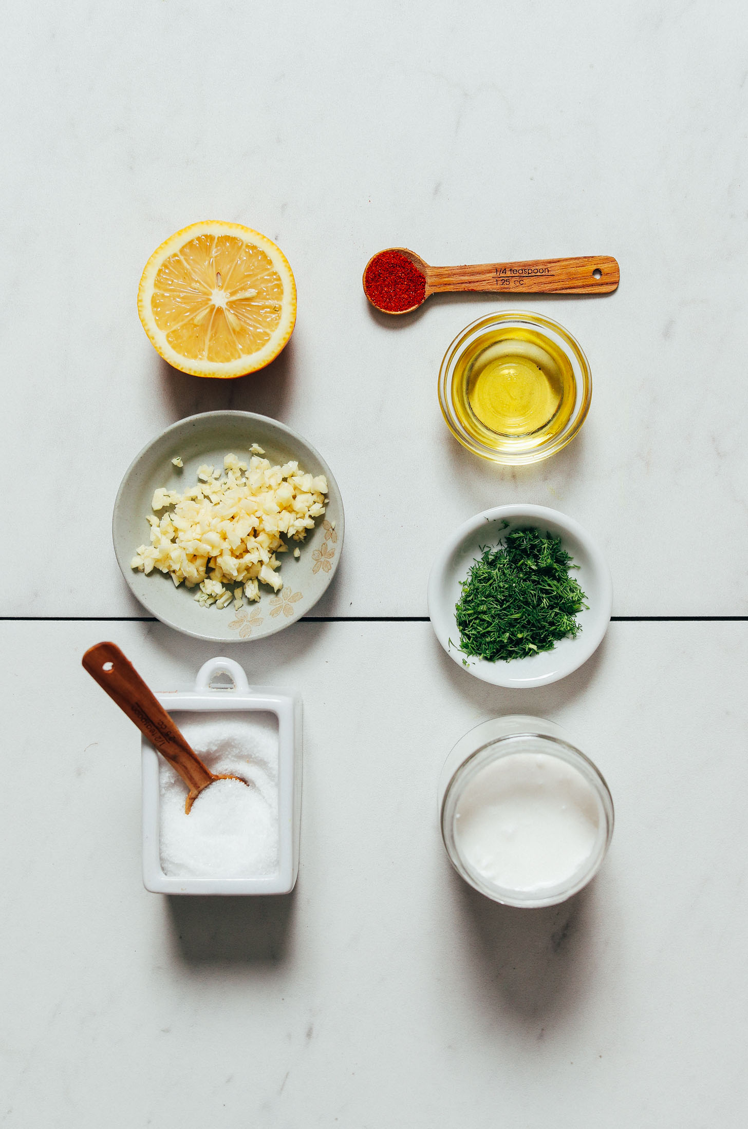 Halved lemon, minced garlic, salt, coconut yogurt, dill, olive oil, and cayenne for making our Zesty Dill Yogurt Sauce recipe