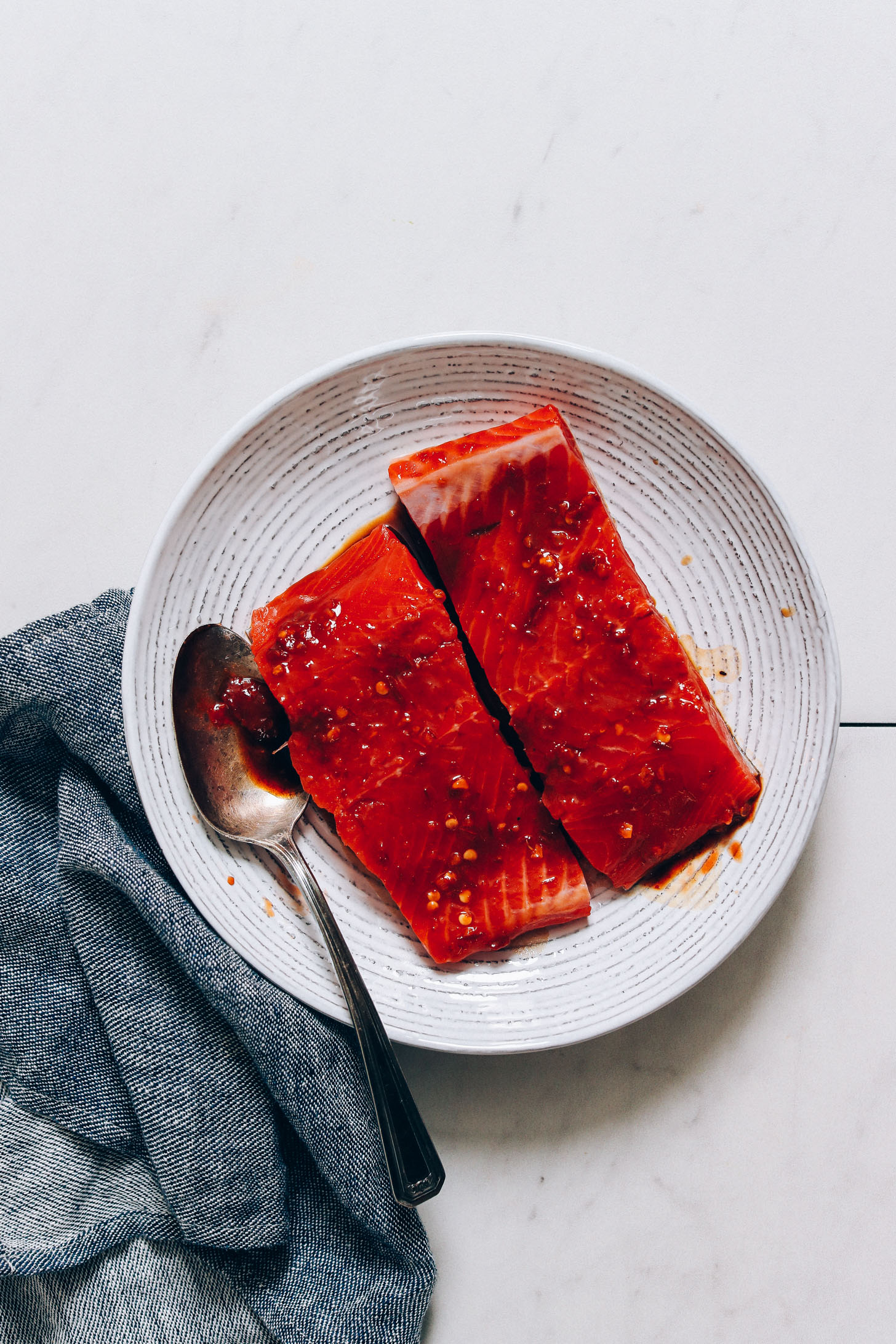 Two salmon filets marinating in coconut aminos, sea salt, and chili garlic sauce in a bowl