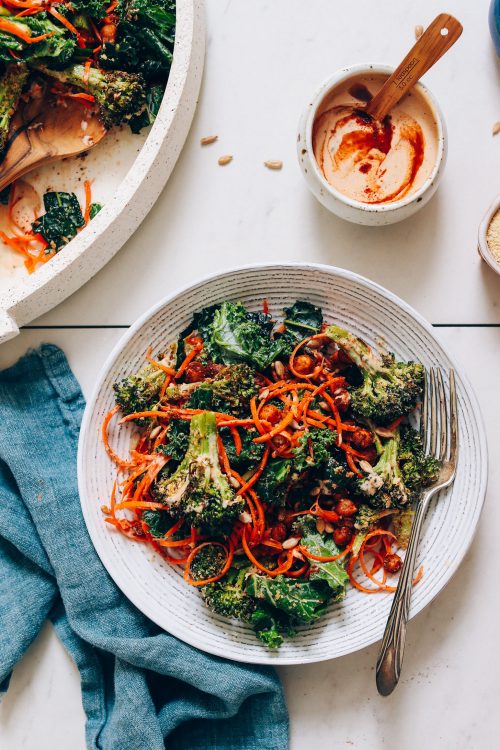 Bowl of smoky chipotle dressing beside a plate and platter of chickpea kale salad