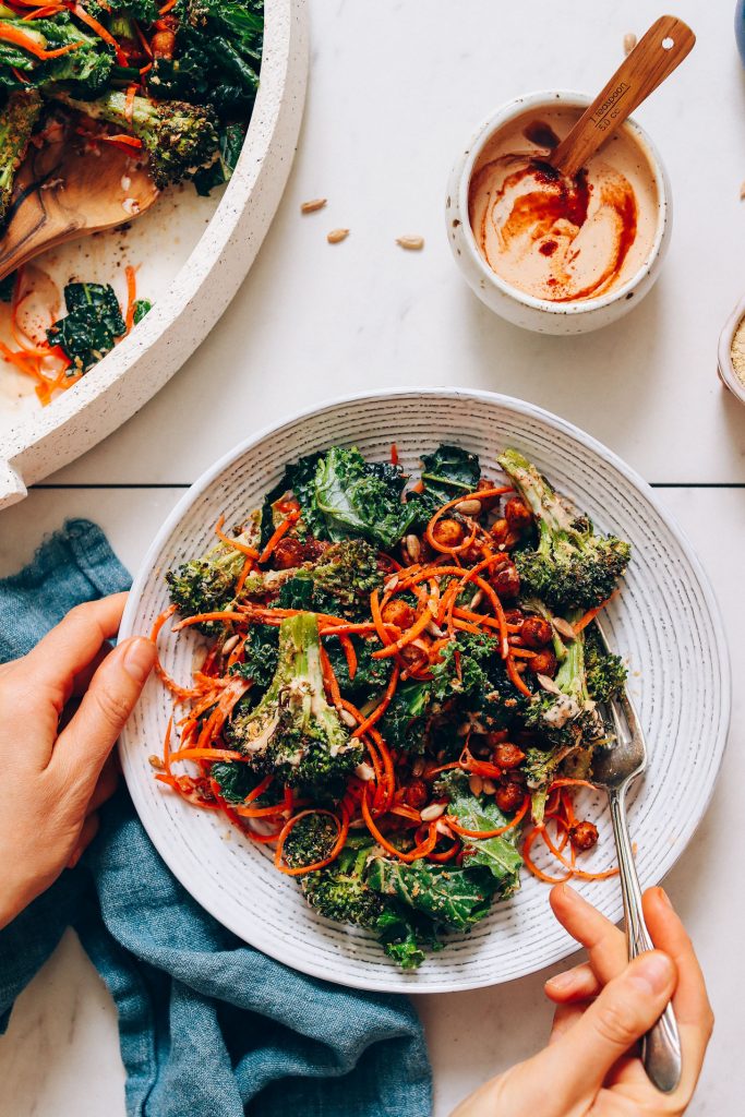 Holding a fork in a bowl of Cheesy Roasted Broccoli and Chickpea Kale Salad