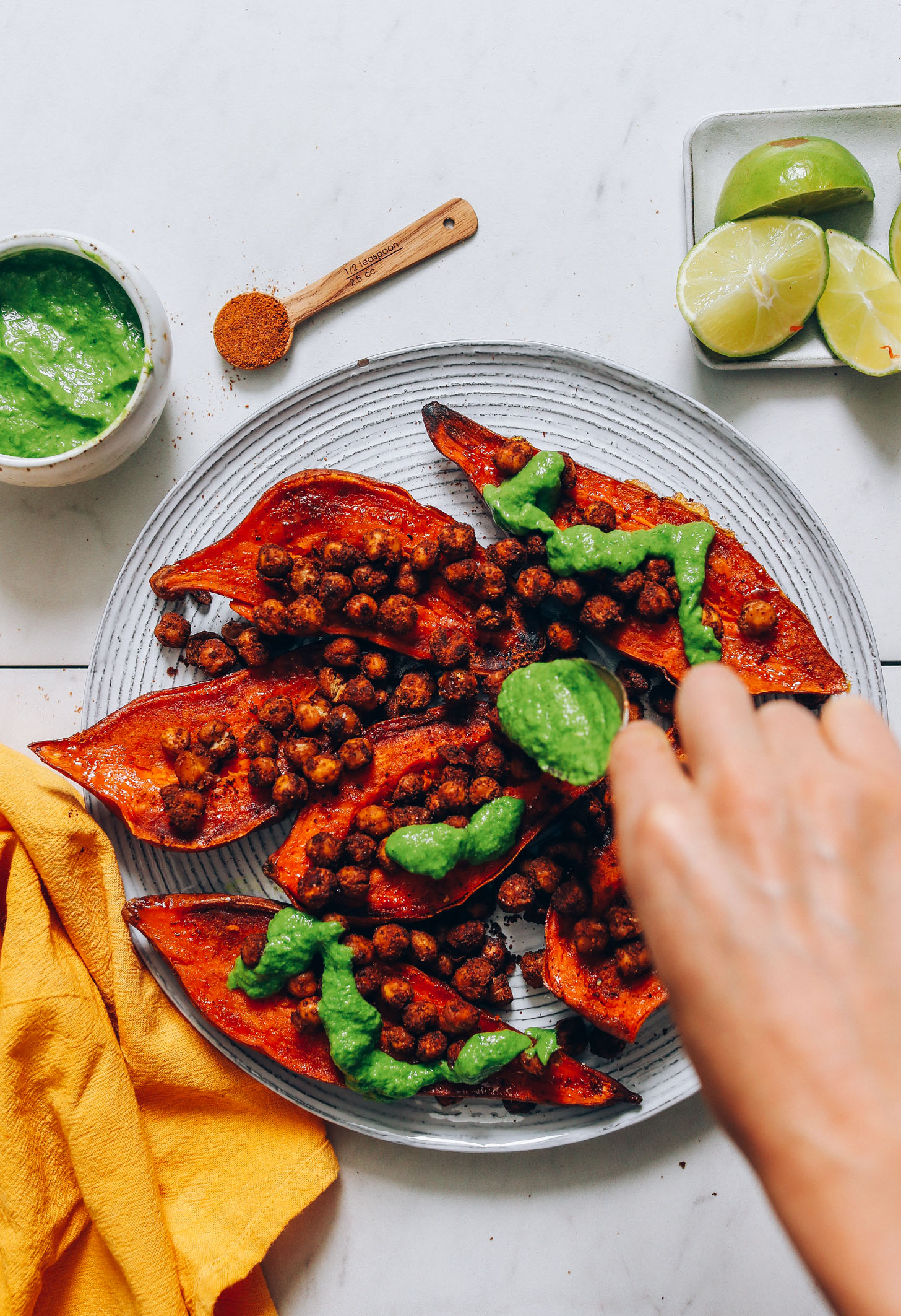 Drizzling green chutney onto a plate of stuffed sweet potatoes