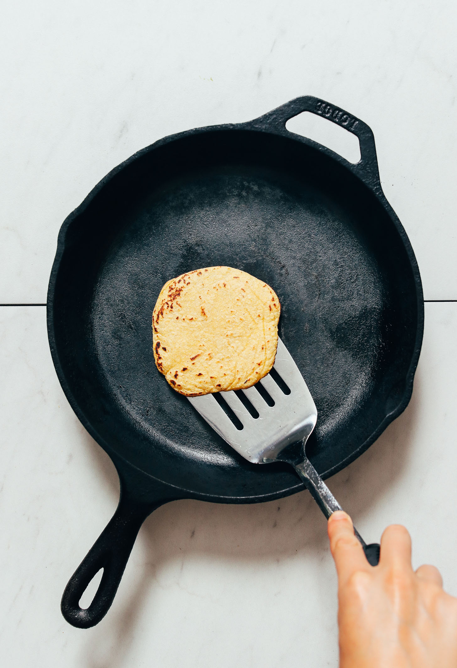 Using a metal spatula to flip a homemade corn tortilla