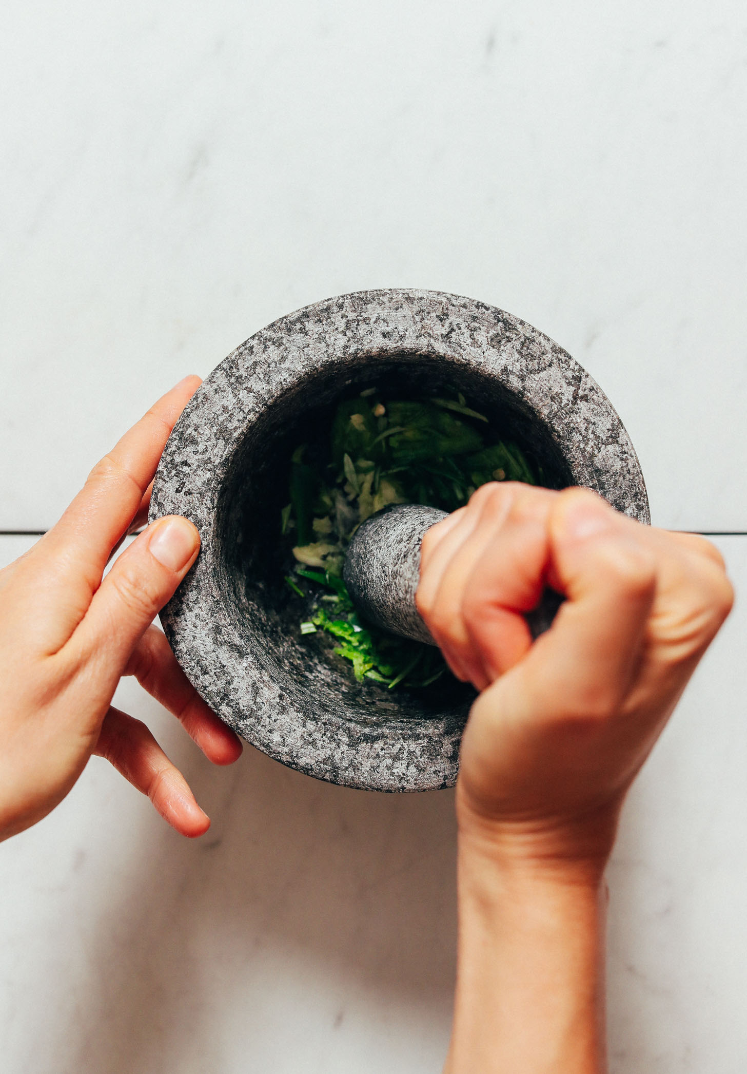 Using a mortar and pestle to crush serrano and garlic for our Rosemary Guacamole recipe