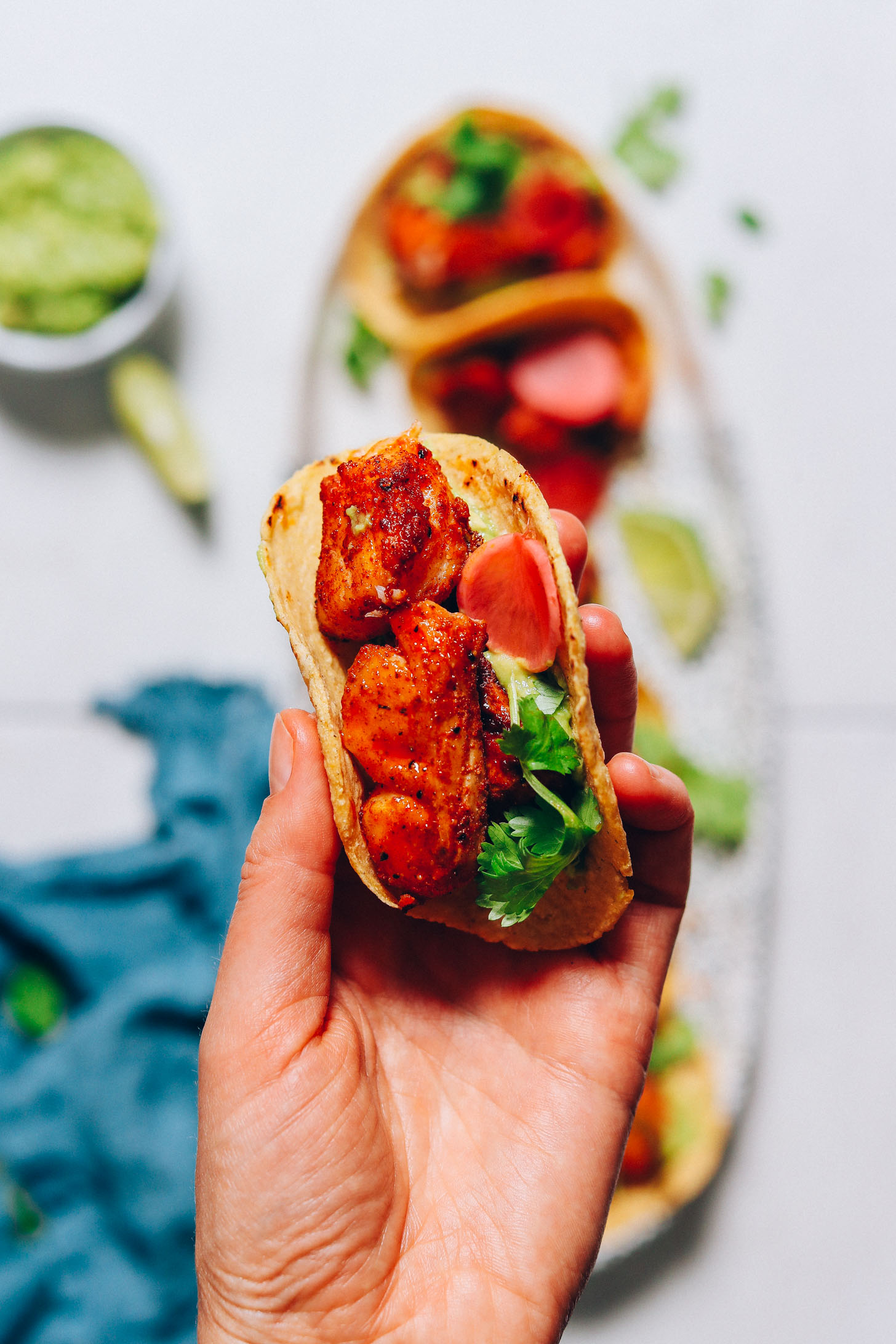 Holding up a Spicy Baked Fish Taco above a tray with more tacos