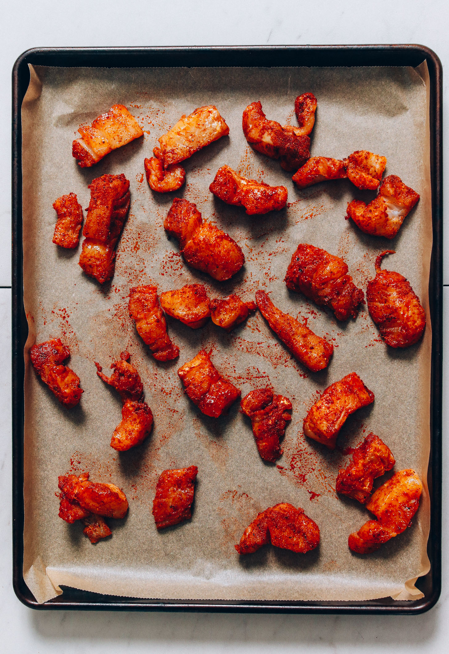 Parchment-lined baking sheet with pieces of cod coated in spices