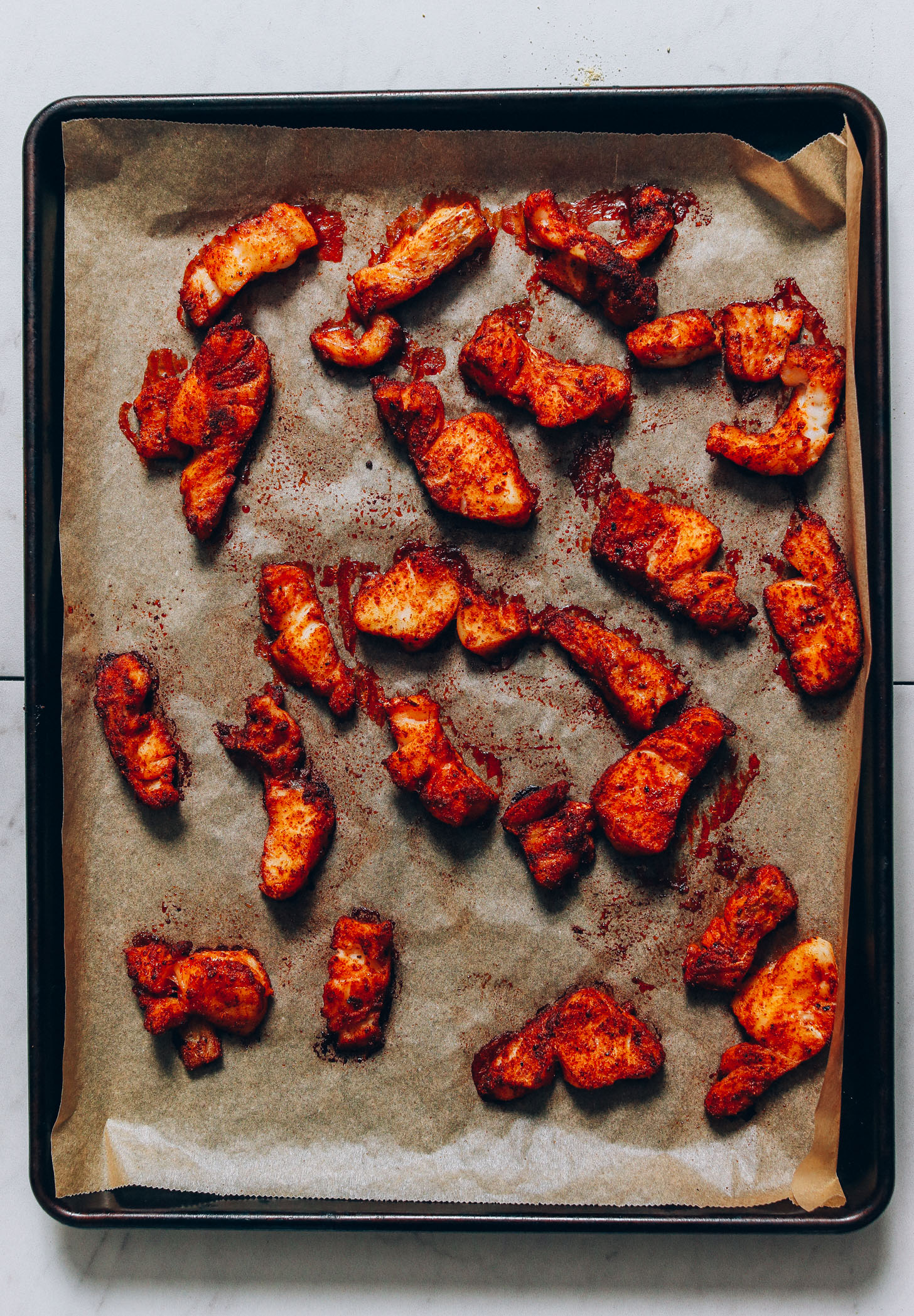 Parchment-lined baking sheet with freshly baked cod coated in spices for making Fish Tacos