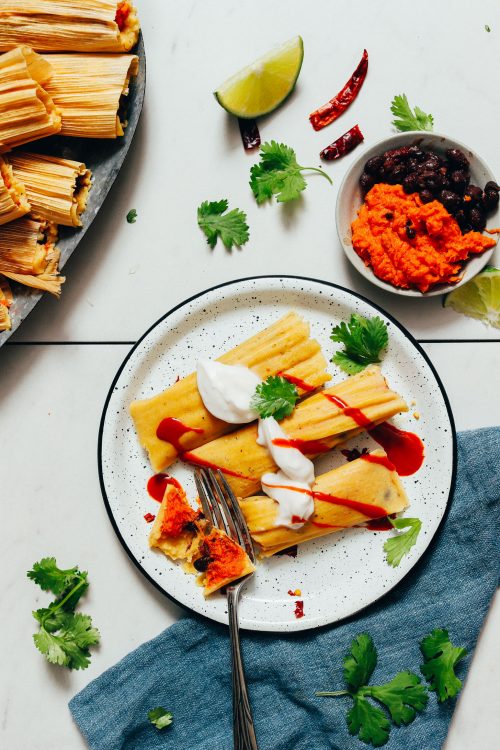 Plate of sweet potato black bean tamales topped with vegan sour cream and sriracha