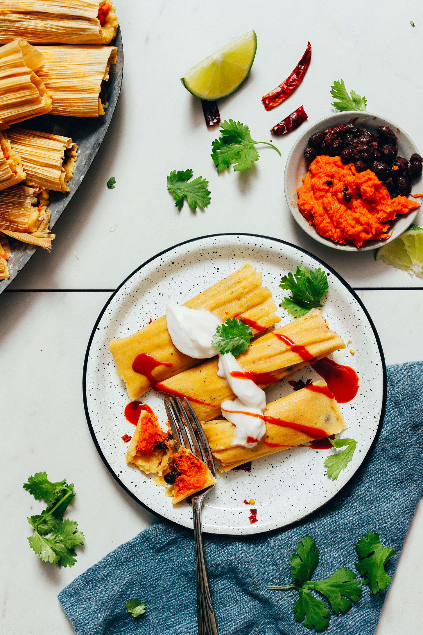 Plate of sweet potato black bean tamales topped with vegan sour cream and sriracha