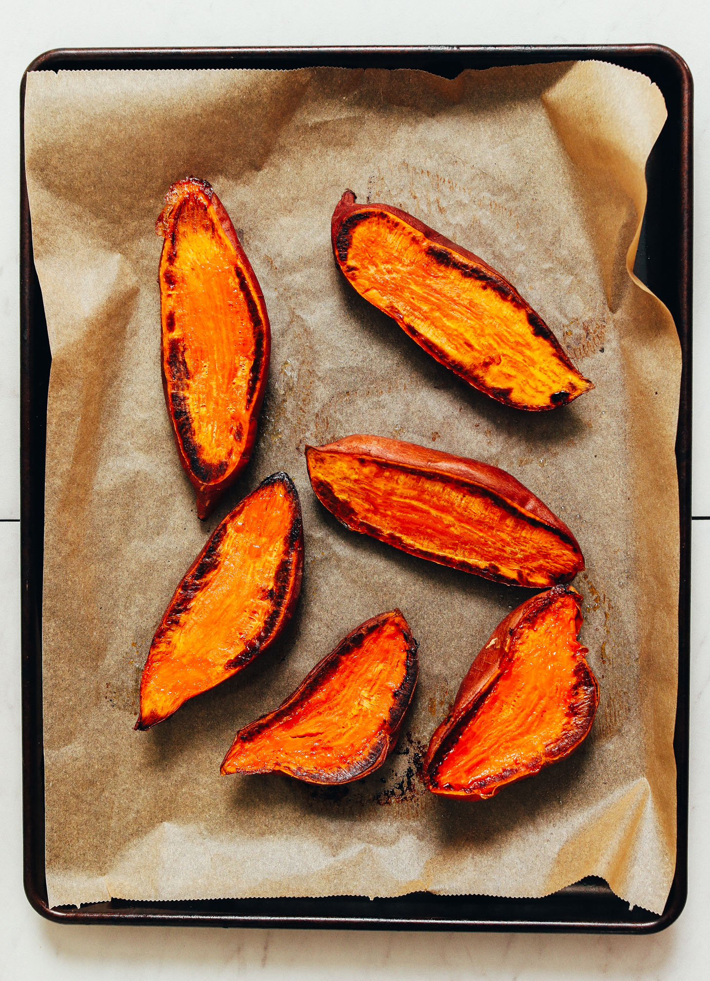 Parchment-lined baking sheet of halved and roasted sweet potatoes