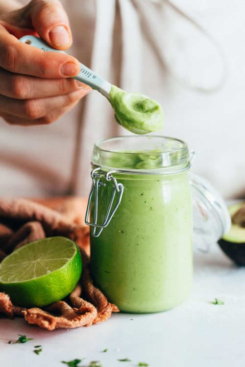 Holding a mini measuring spoon over a halved lime and jar of Avocado Aioli