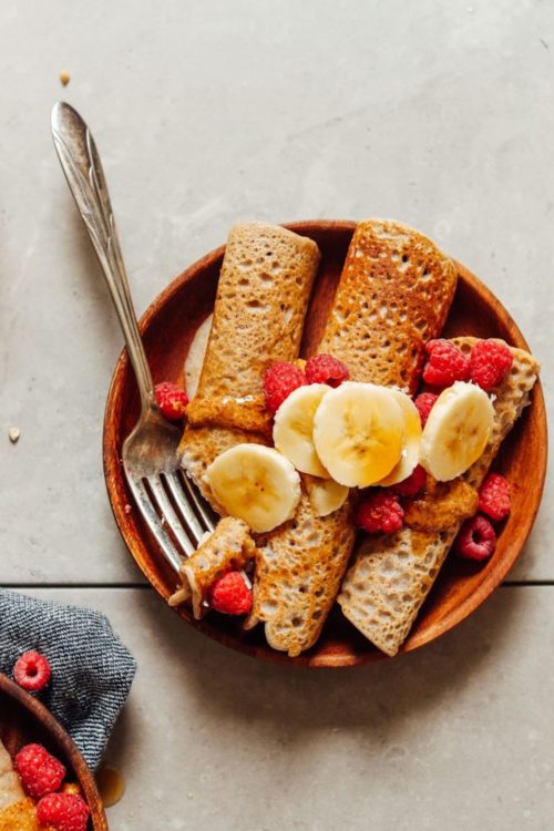 A plate of three buckwheat crepes with berries and bananas