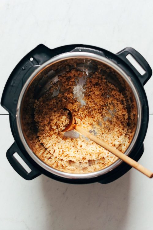 Wooden spoon in an instant pot with brown rice and water