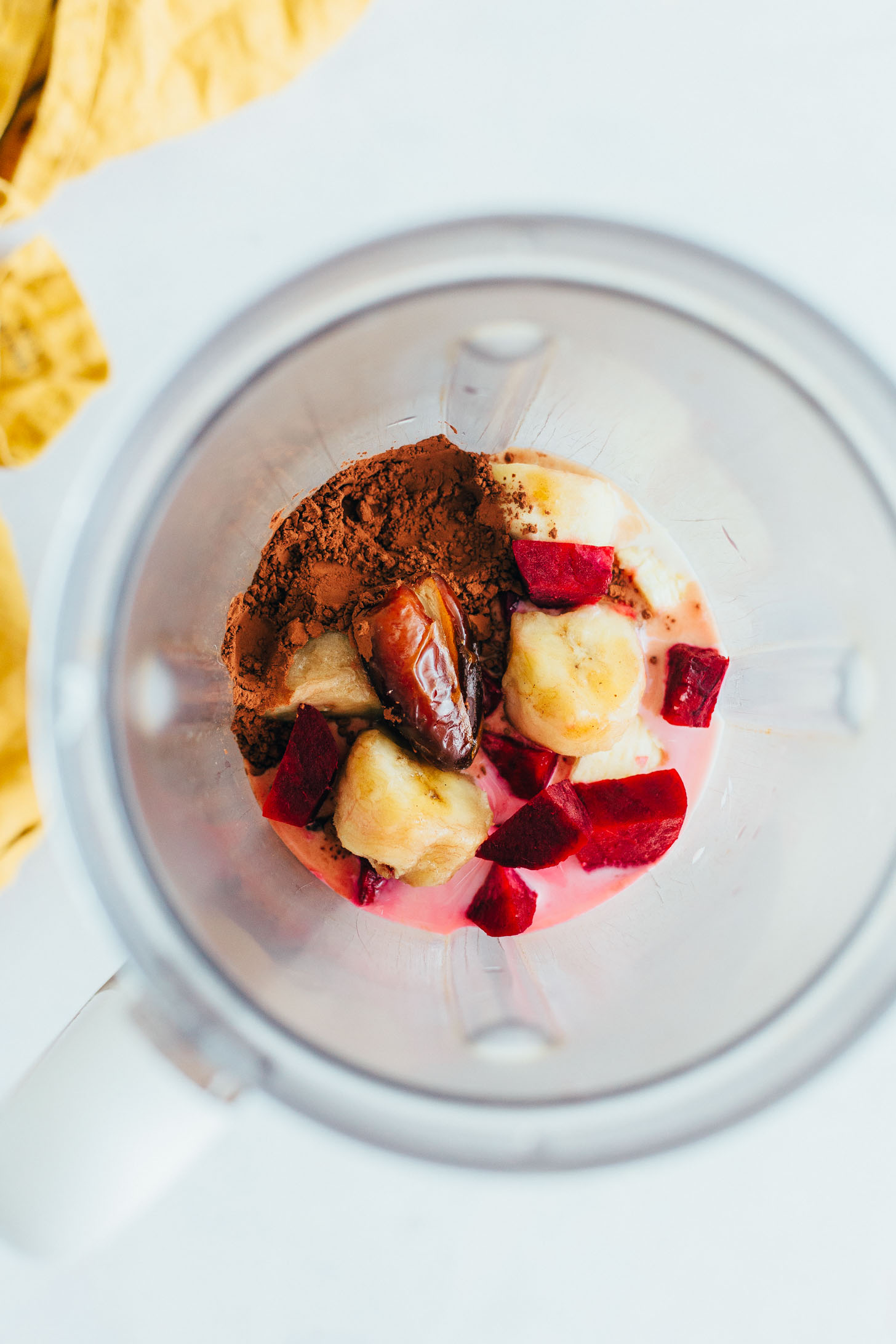Blender filled with dairy-free milk, banana, dates, beets, and cacao powder