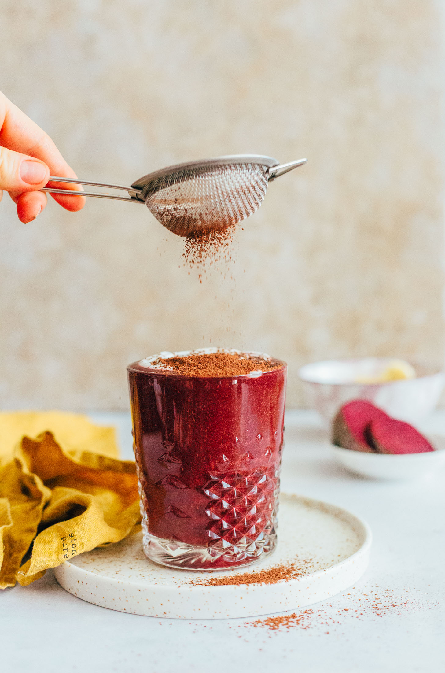 Sprinkling cacao powder over a glass filled with our beet smoothie recipe