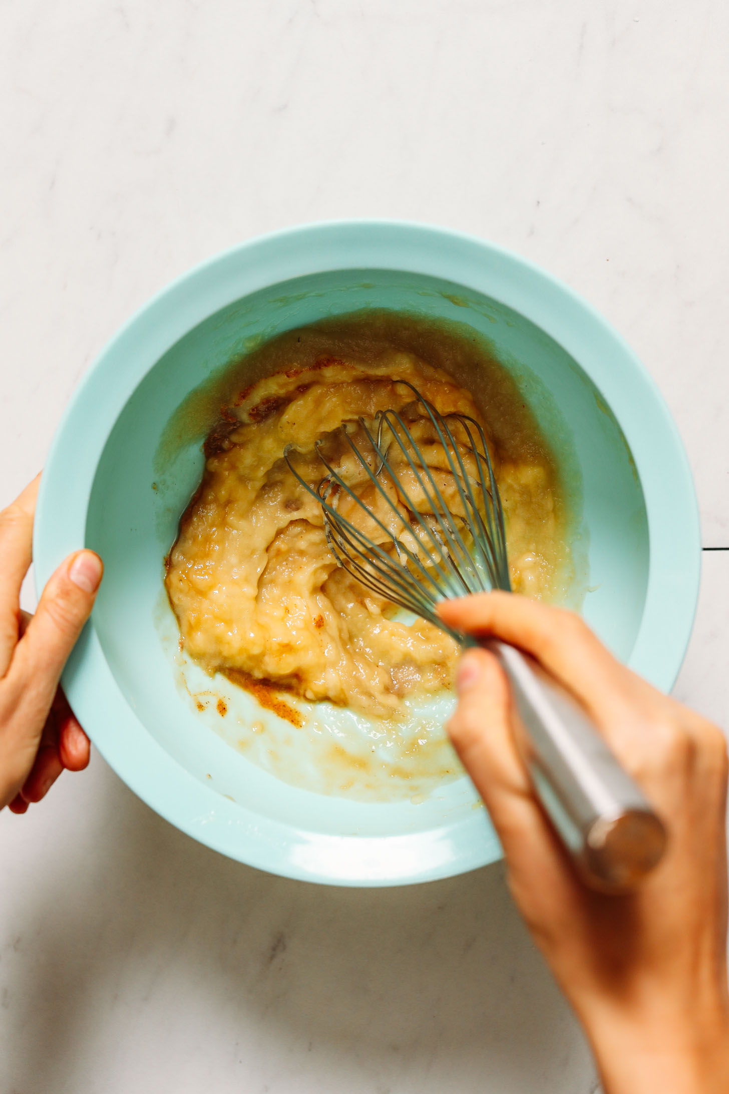 Whisking banana, applesauce, and vanilla in a mixing bowl
