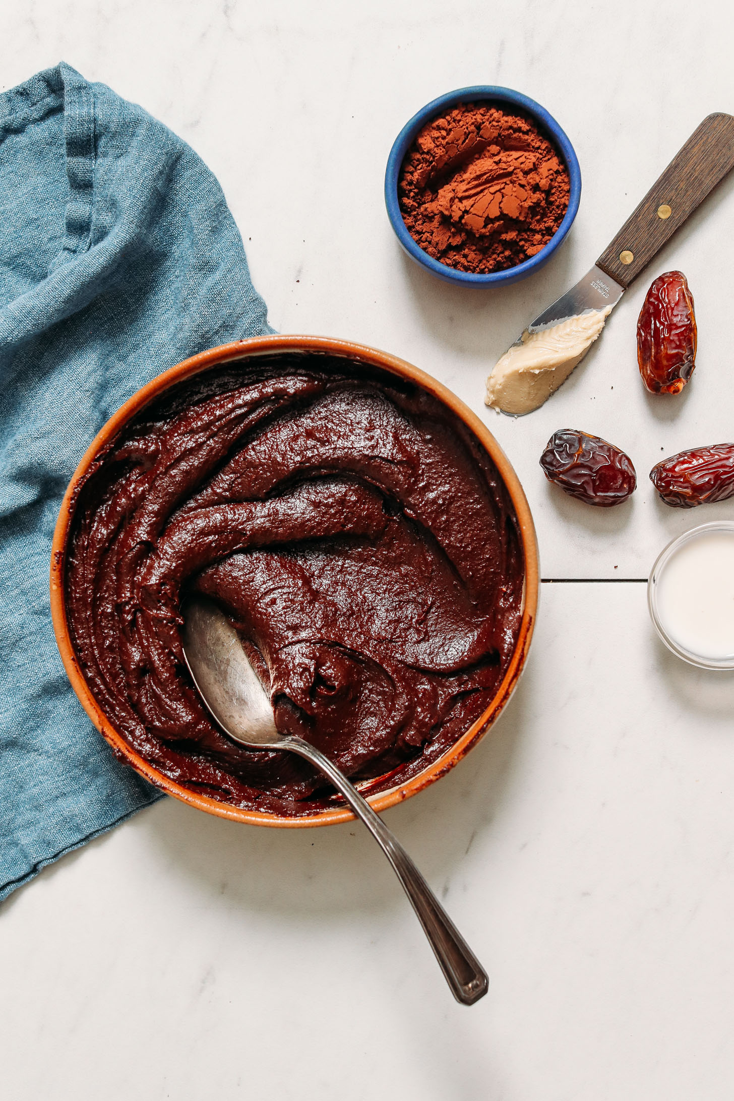 Bowl of date-sweetened vegan chocolate frosting next to ingredients used to make it