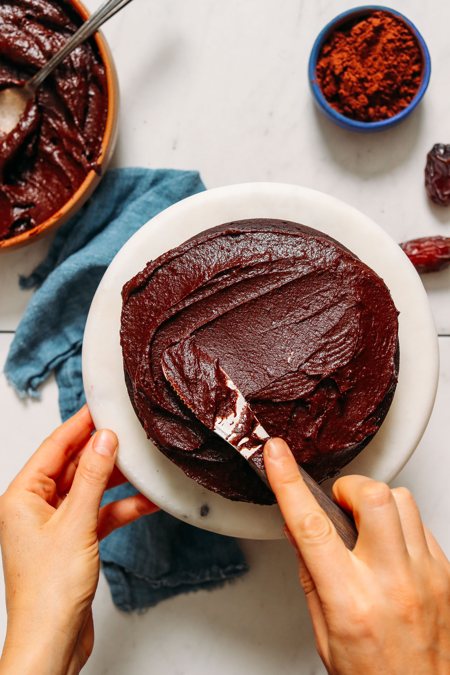 Using a knife to spread Creamy Cashew Butter Chocolate Frosting onto a three tier Gluten Free Chocolate Cake