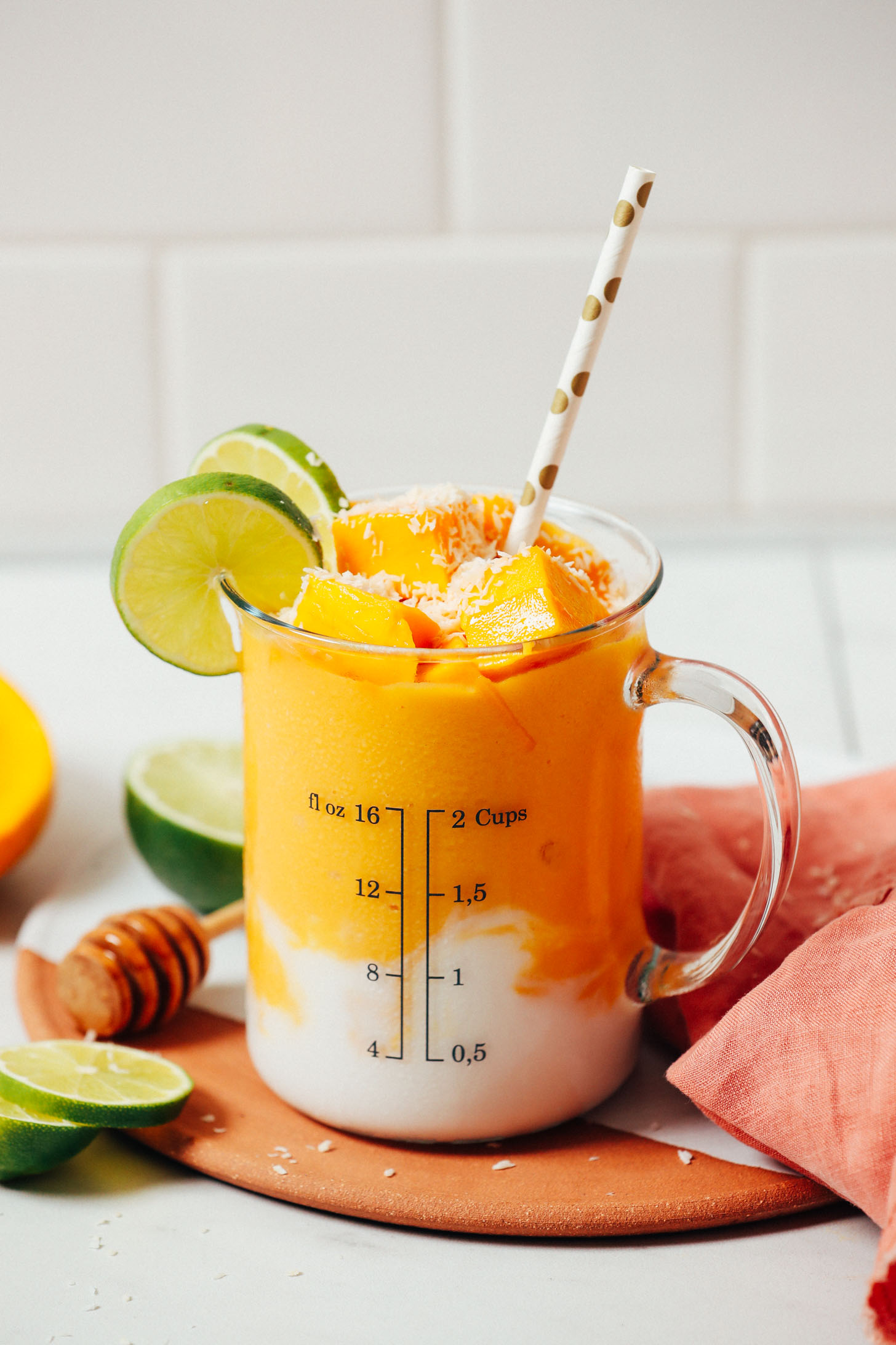 Measuring glass of our Mango Lassi Smoothie topped with coconut, mango chunks, and lime