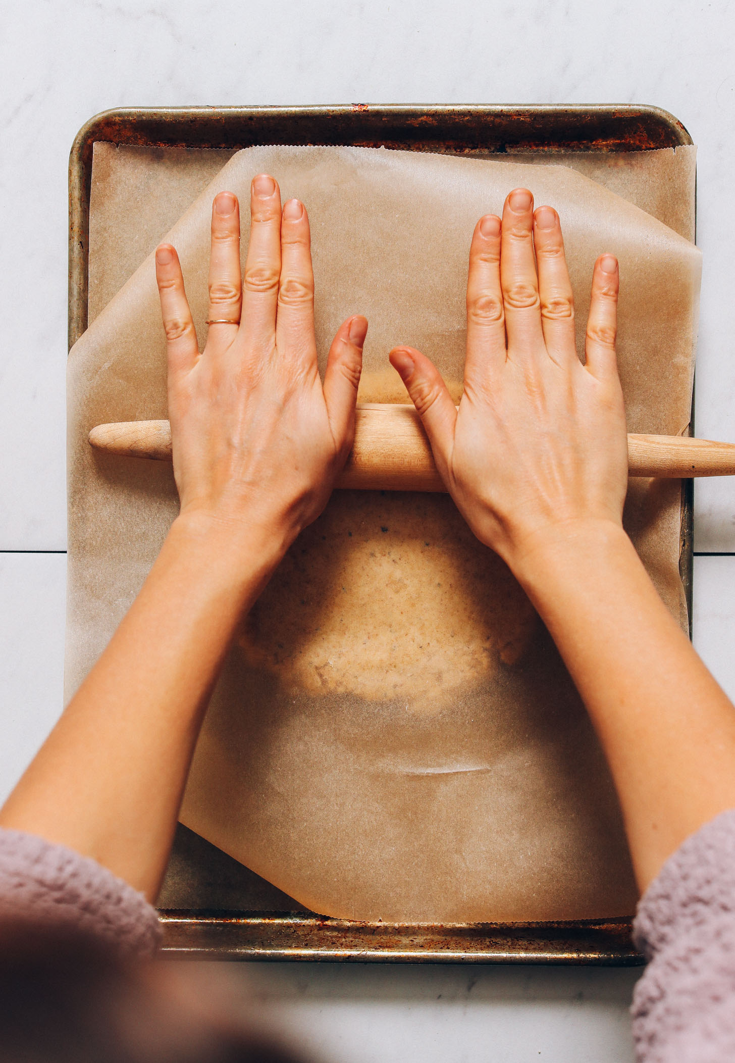 Using a rolling pin to roll out pizza dough between sheets of parchment paper