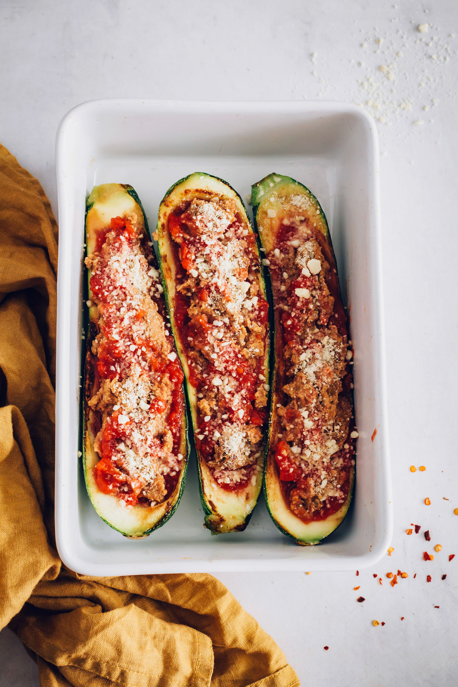 Baking pan with three Zucchini Boats sprinkled with vegan parmesan
