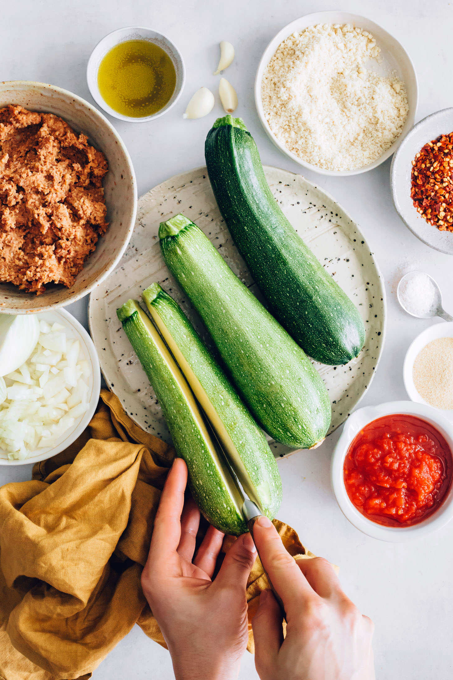 Slicing into a zucchini surrounded by vegan sausage, onion, vegan parmesan, red pepper flakes, and marinara
