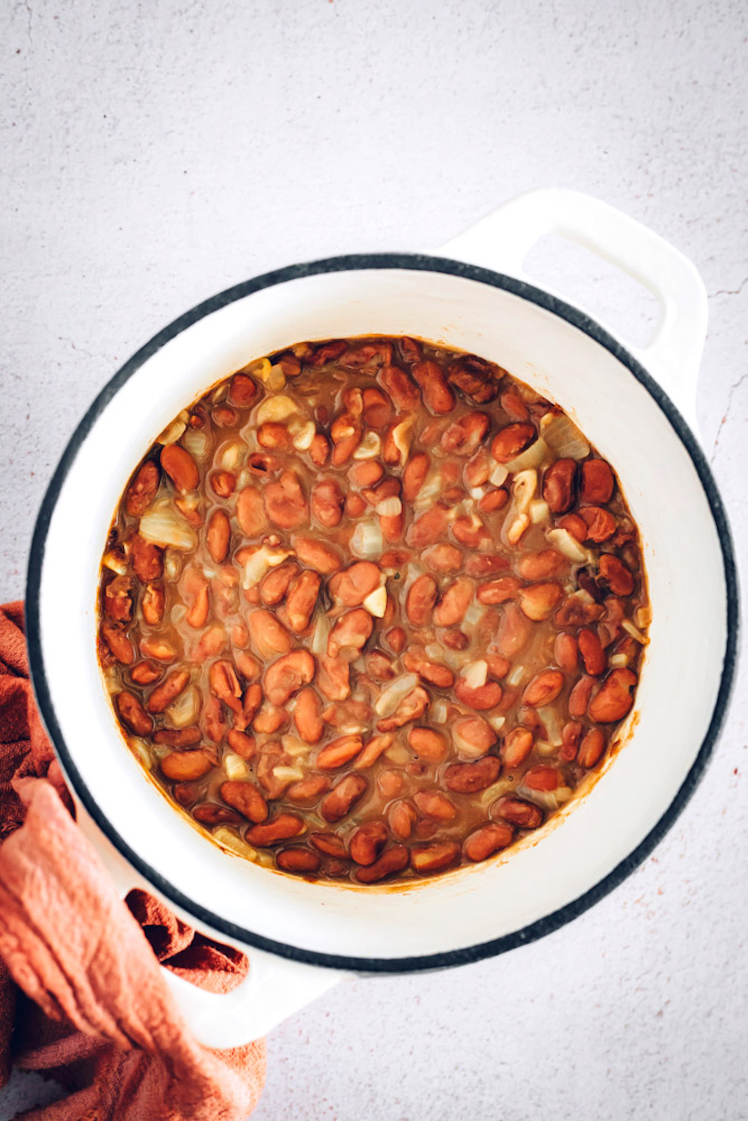 Dutch oven of cooked pinto beans seasoned with onion and garlic