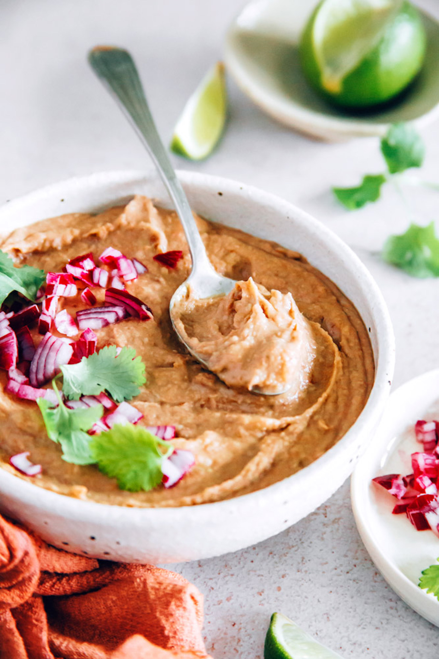 Spoon resting in a bowl of vegan Refried Beans topped with red onion and cilantro
