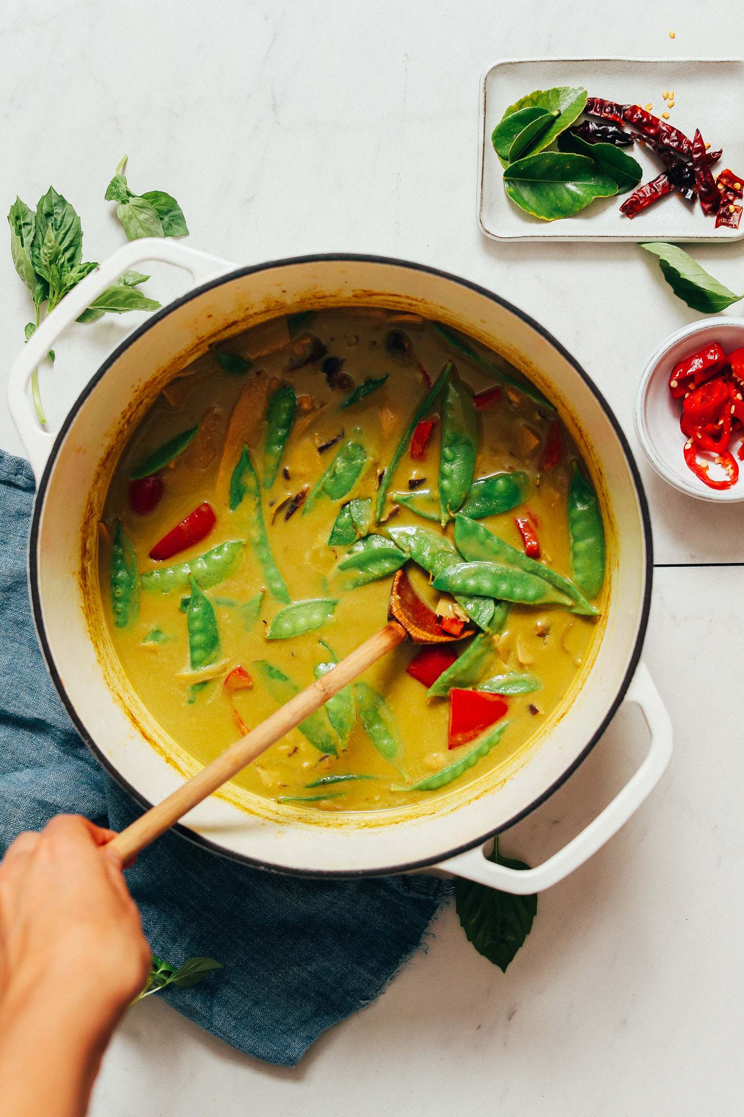 Chilies, kaffir lime leaves, and basil next to a pot of green curry