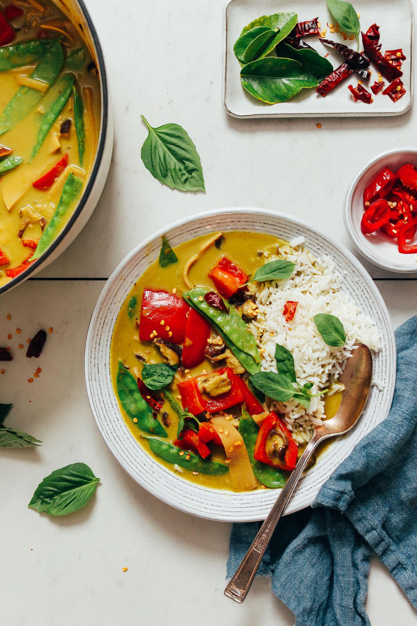 Bowl of white rice and Thai green curry next to a pot of more curry and ingredients used to make it