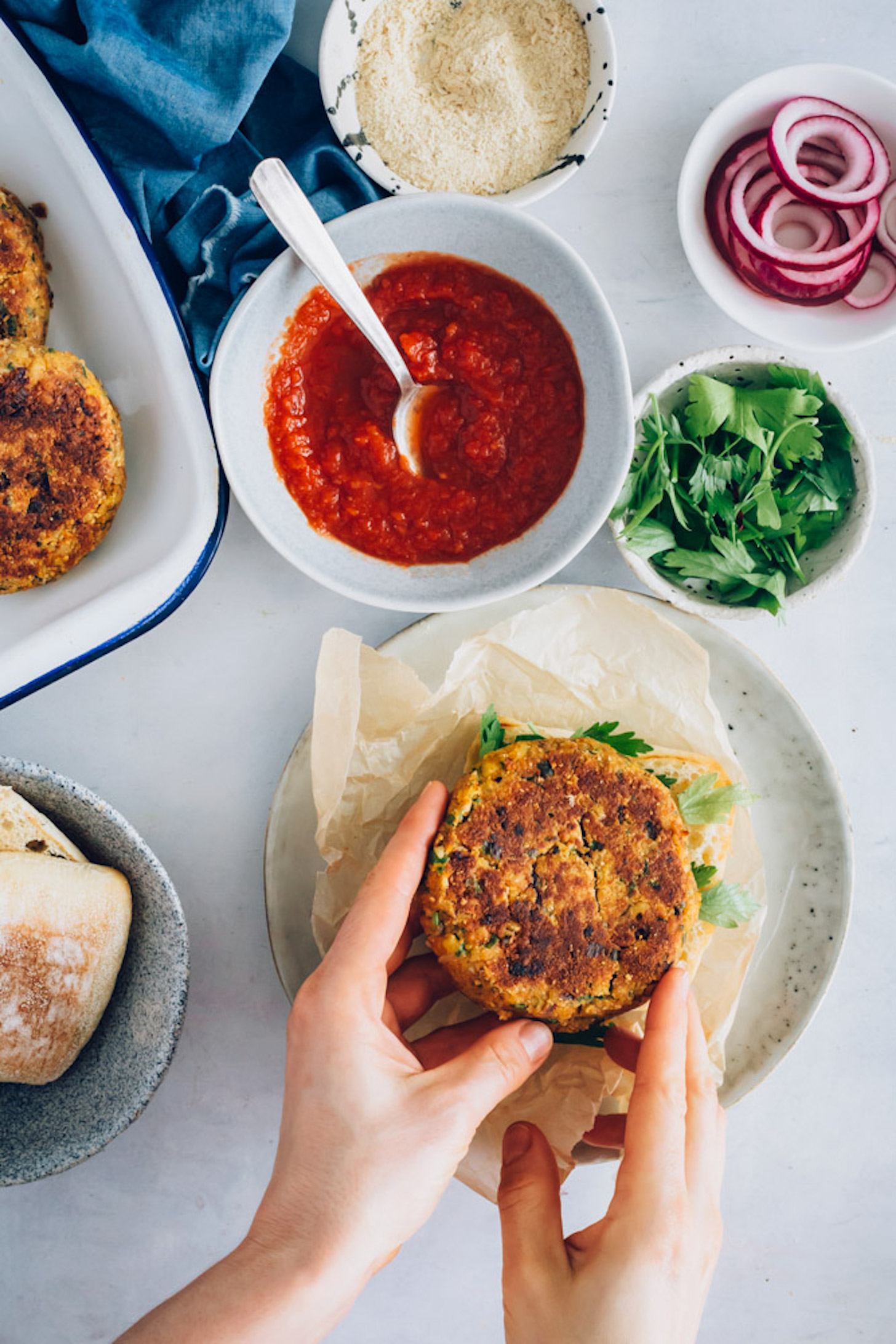 Vegan Pizza Burgers next to marinara sauce, parsley, red onion, and vegan parmesan