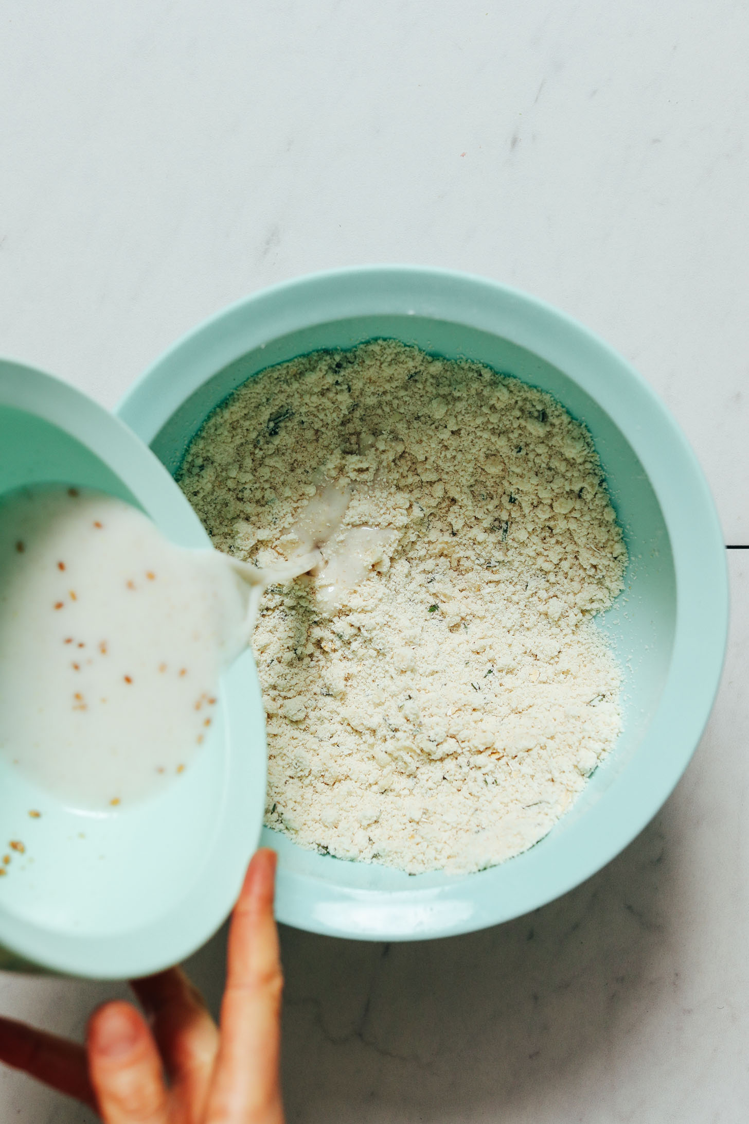 Pouring almond milk and flax mixture into coconut oil and flour bowl