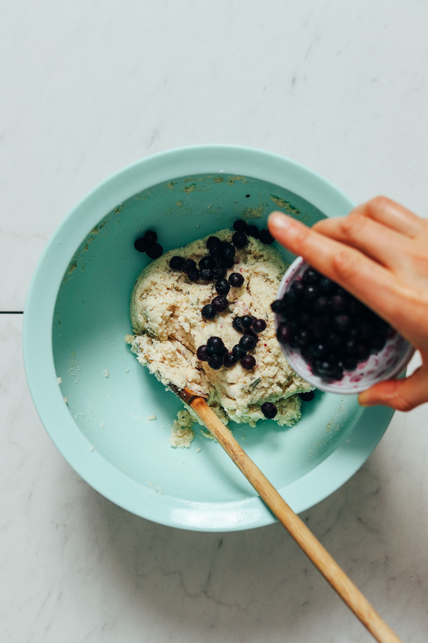 Pouring wild blueberries from a small bowl into a bowl of scone dough