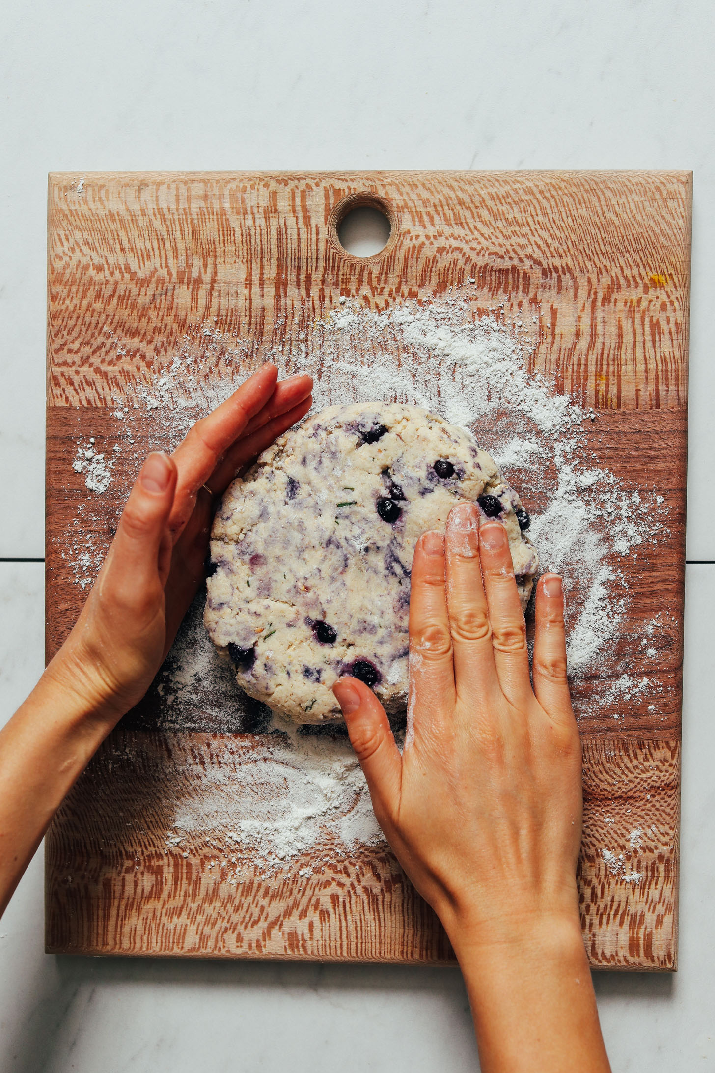 Hands shaping scone dough on a wood cutting board