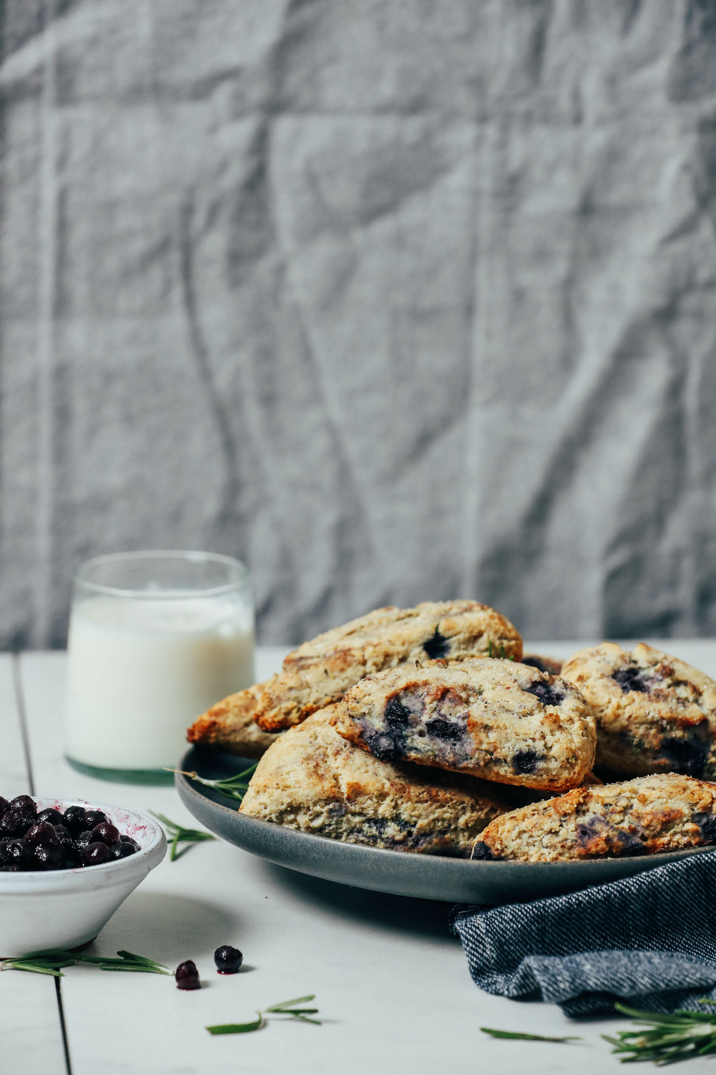 Wild blueberries, rosemary, and almond milk next to a large plate of Gluten Free Scones