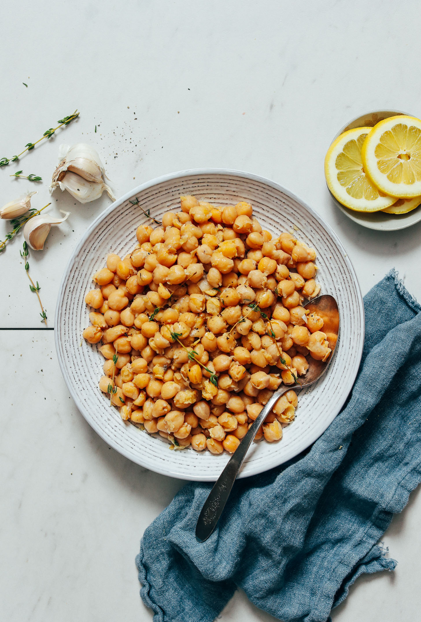Vintage spoon in a bowl of Instant Pot Chickpeas next to garlic, thyme, and lemon slices