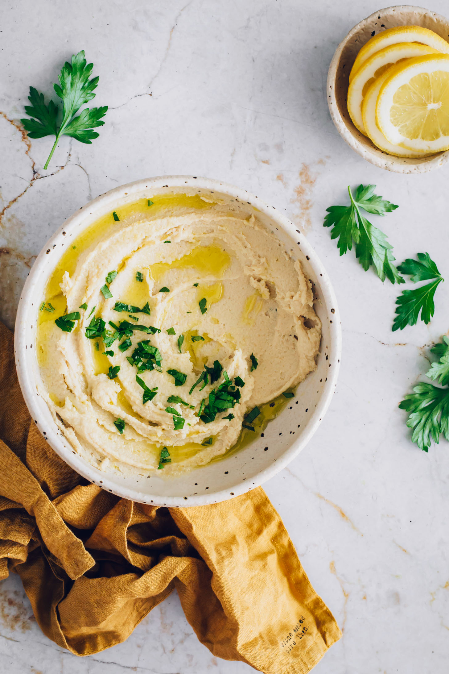 Top down shot of a bowl of vegan ricotta cheese with lemon slices and fresh parsley