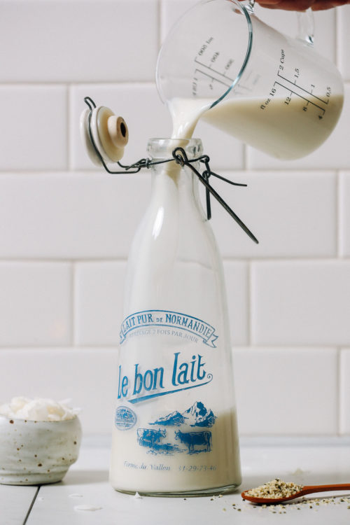 Pouring homemade coconut hemp milk into a glass milk jug