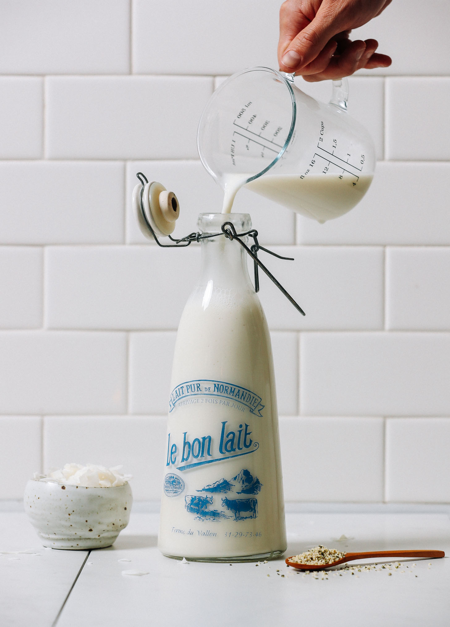 Coconut flakes and hemp seeds next to a jug of homemade dairy-free milk