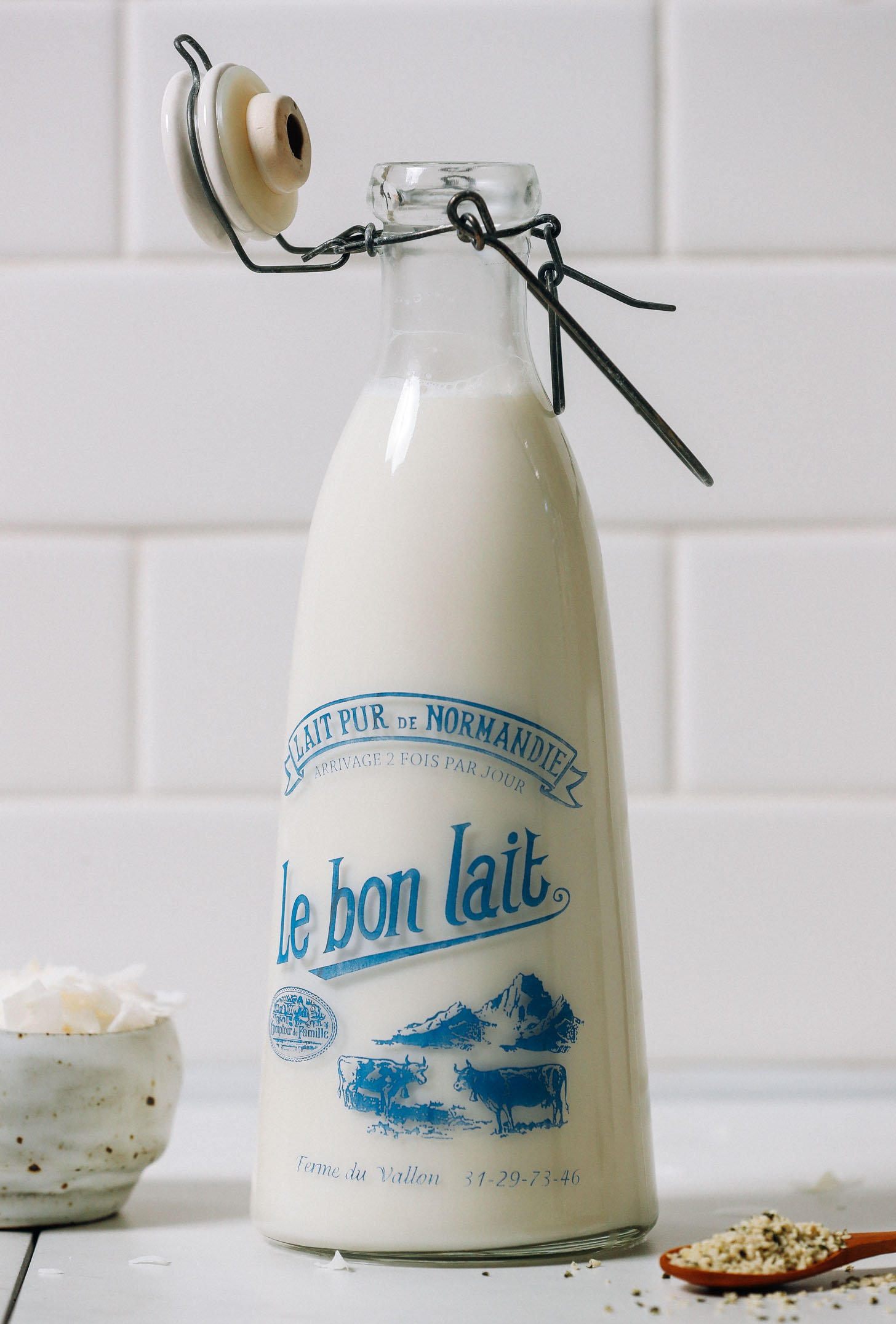 Jug of homemade vegan milk next to coconut flakes and hemp seeds