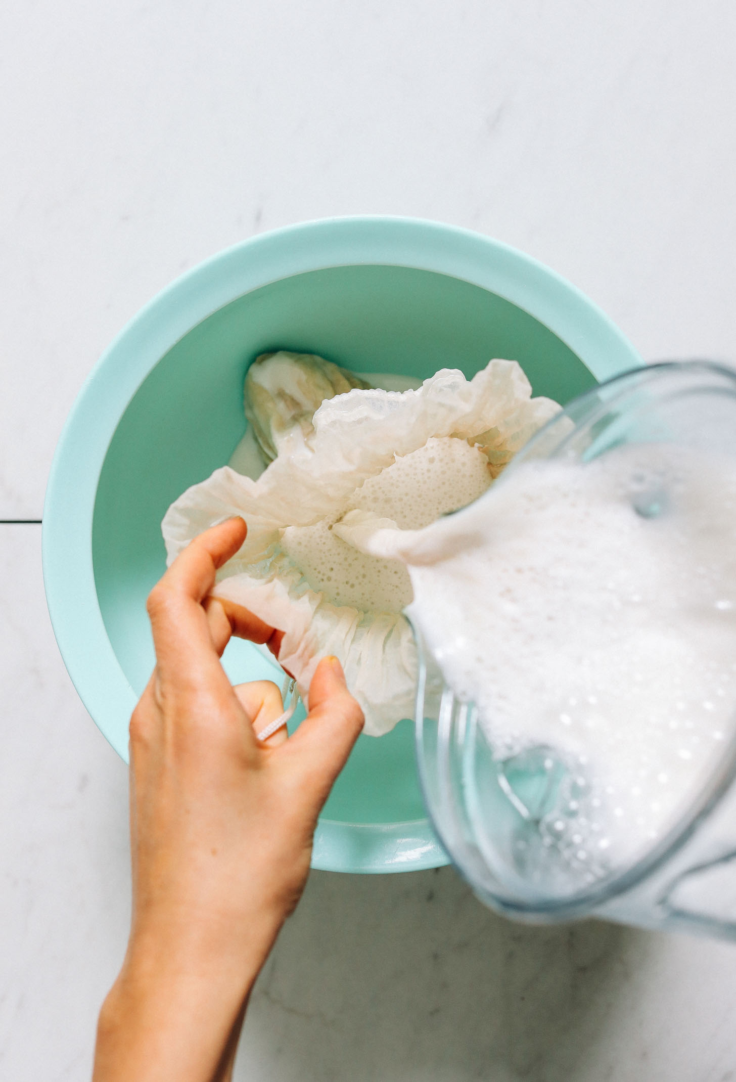 Pouring Coconut Hemp Milk through a nut milk bag into a bowl