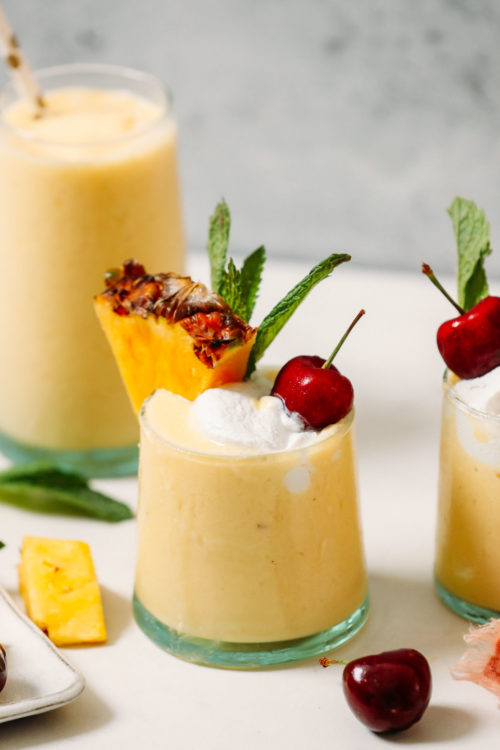 Glasses of our Piña Colada Smoothie topped with coconut whipped cream and cherries