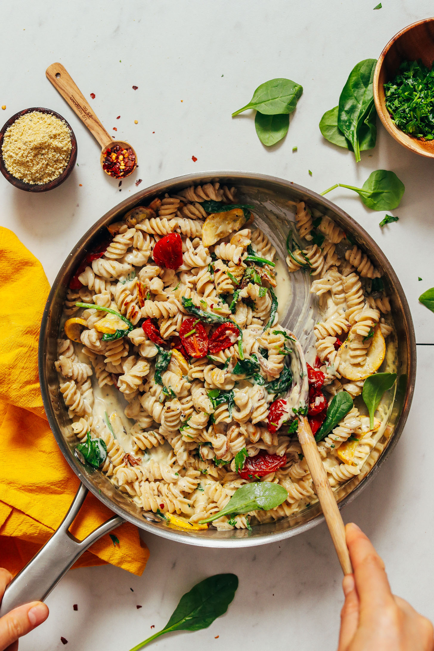 Using a wooden spoon to stir a pan of Creamy Vegan White Pasta with Summer Vegetables